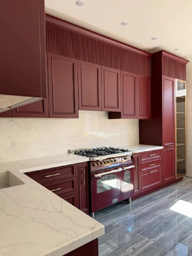 Luxury custom burgundy kitchen remodel in Orange County featuring a premium gas range and seamless stone backsplash.